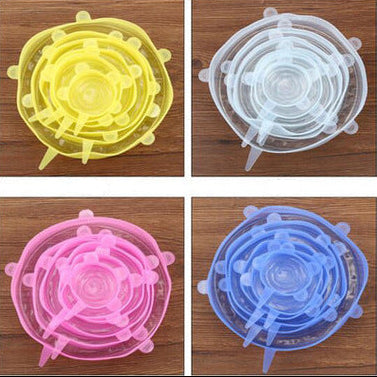 Four silicone stretch lids in yellow, clear, pink, and blue on a wooden surface.
