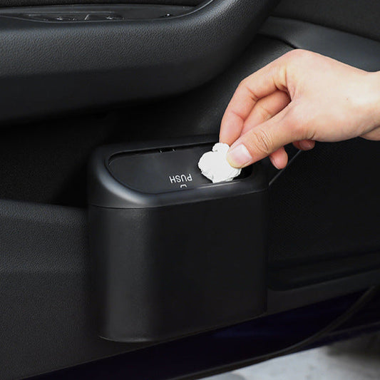 Hand placing trash into a black car trash can on a dark background